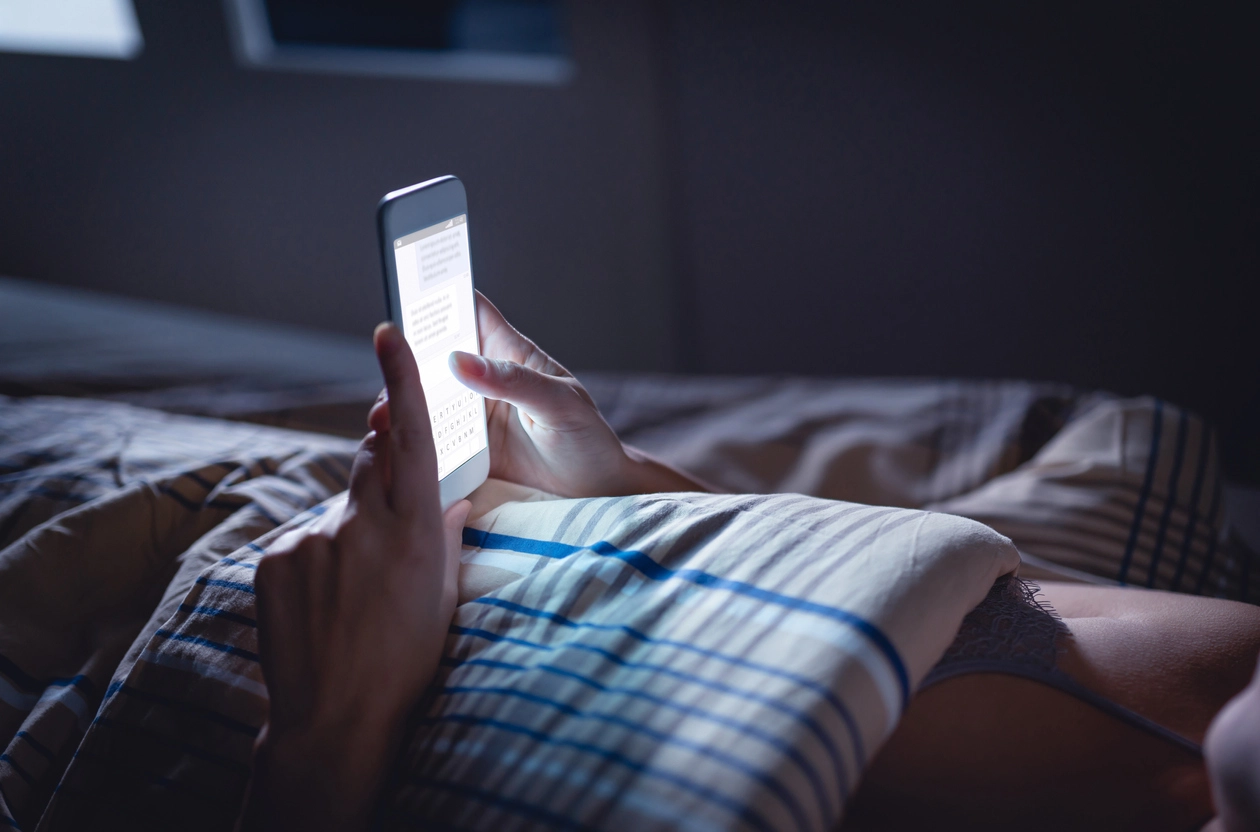 Donna sdraiata a letto che utilizza lo smartphone